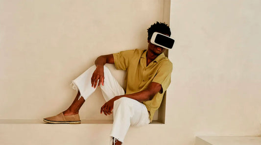 Man wearing light summer outfit with tan leather slippers, seated on a minimal stone bench